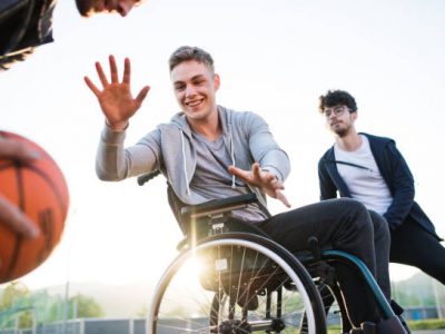 6 A boy in wheelchair with two teenager friends playing basketball outside at sunset.
